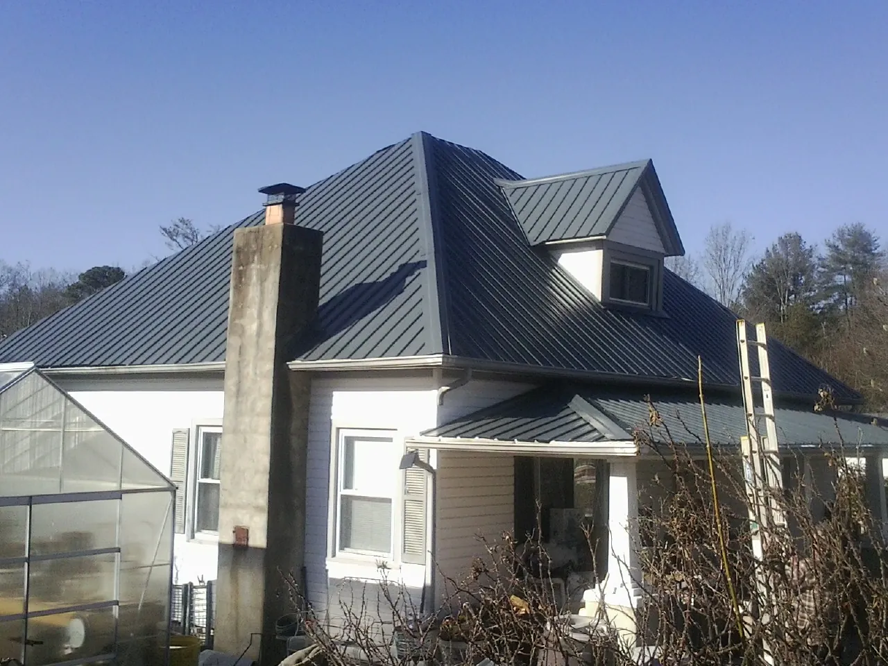 Dark blue standing seam metal roof on a white farmhouse with dormer — Slate & Tile Roof Repair by Roofing Brothers in Canute