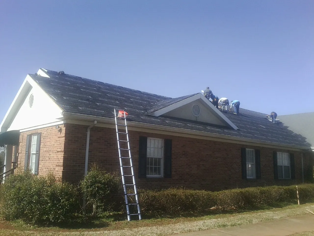 Crew tearing shingles off a brick ranch roof with a ladder set — Emergency Roof Repair work by our crew in Canute