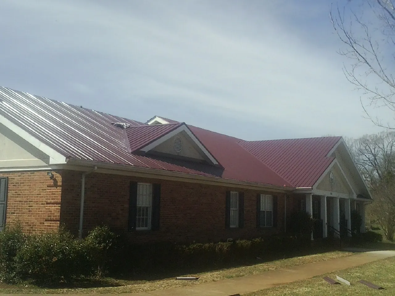 Red metal roof with gabled entries on a long brick building, from a Hail Damage Roof Repair job in Canute