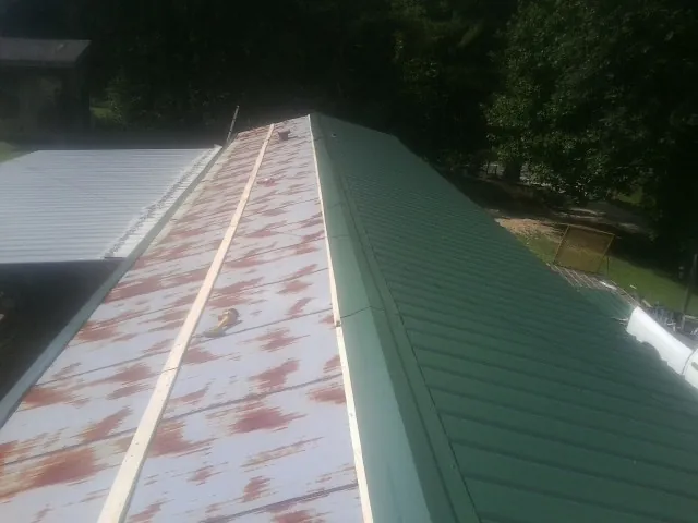 Old rusted panels beside newly installed green metal roofing — Wind Damage Roof Repair by Roofing Brothers in Canute