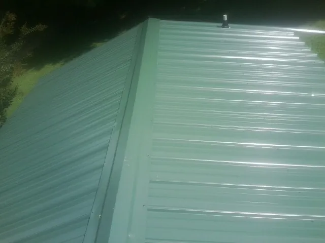 New green metal panels meeting at the ridge of a roof — Flat Roof Repair work by our crew in Canute