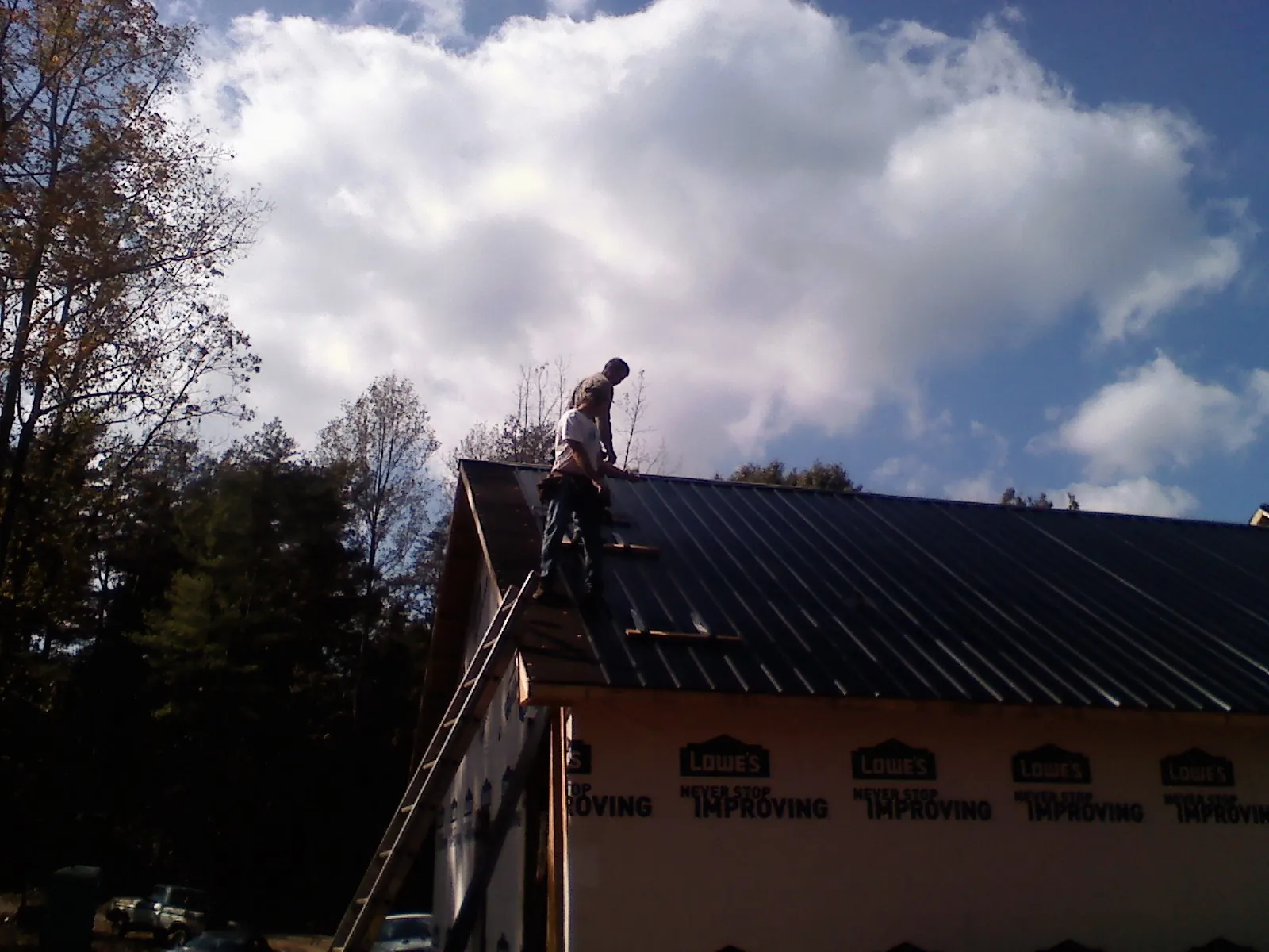 Roofer fastening dark metal panels high against a cloudy sky, from a Roof Inspection job in Canute
