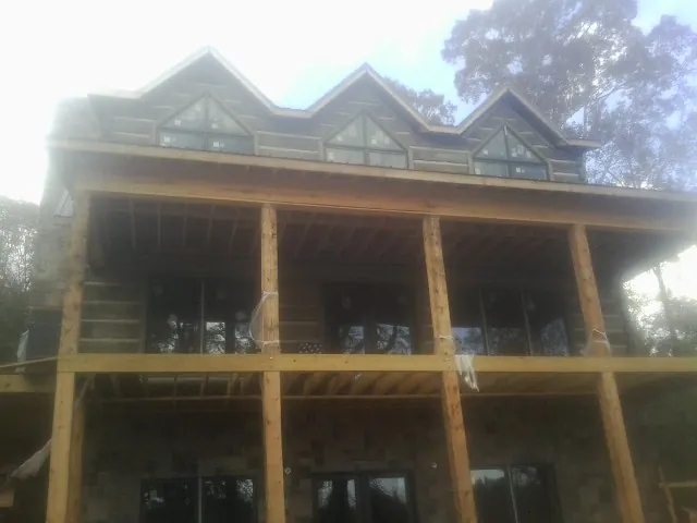 Dormers and porch framing on a large log home under construction — Roof Coating work by our crew in Canute