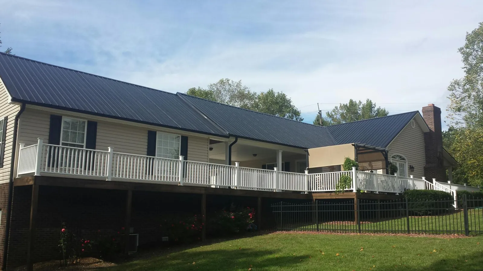 Black metal roof above a long white railed deck on a hillside home in Canute