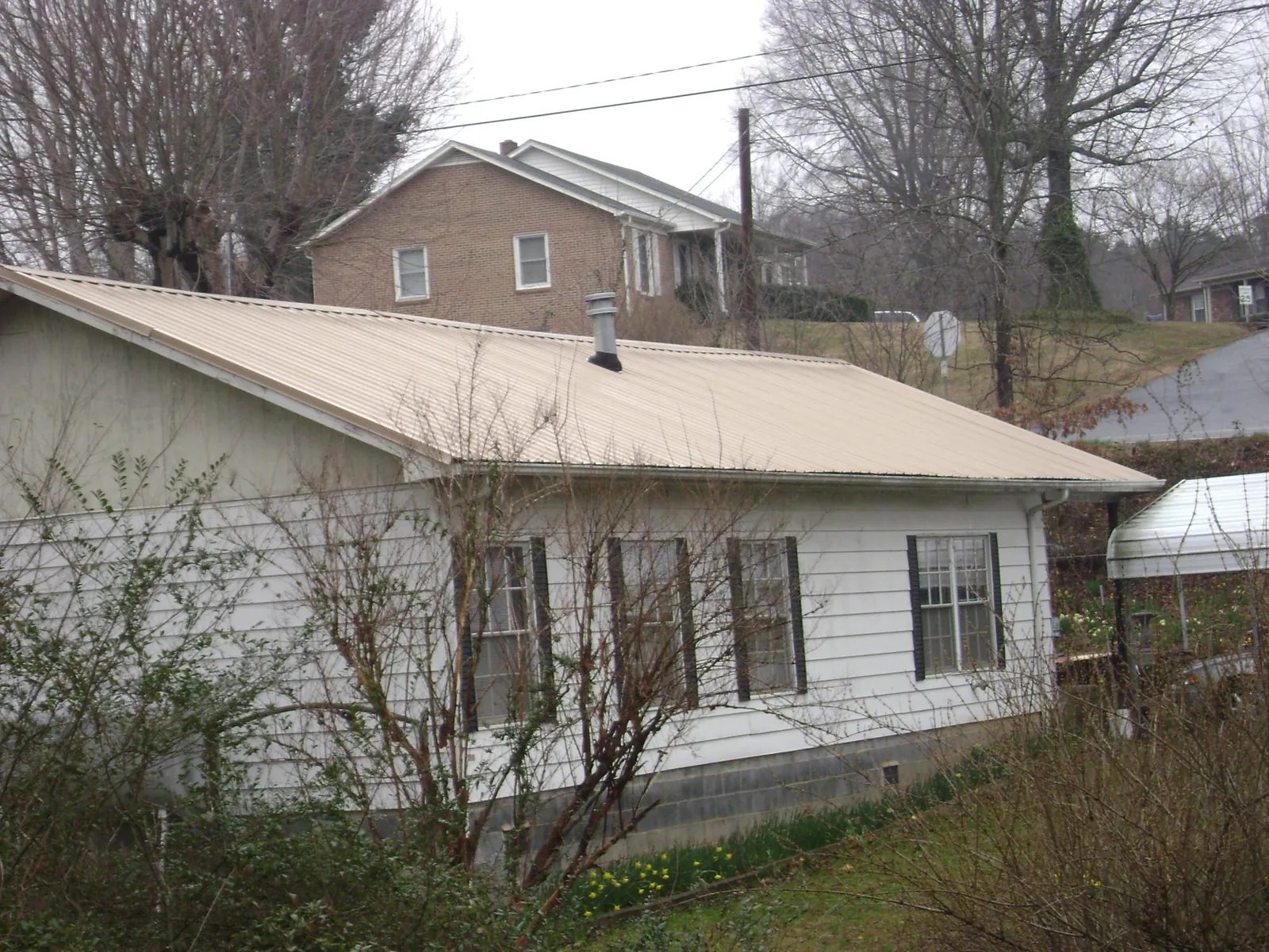 Tan metal roof on a white sided house set into a hillside — Commercial Roofing by Roofing Brothers in Canute