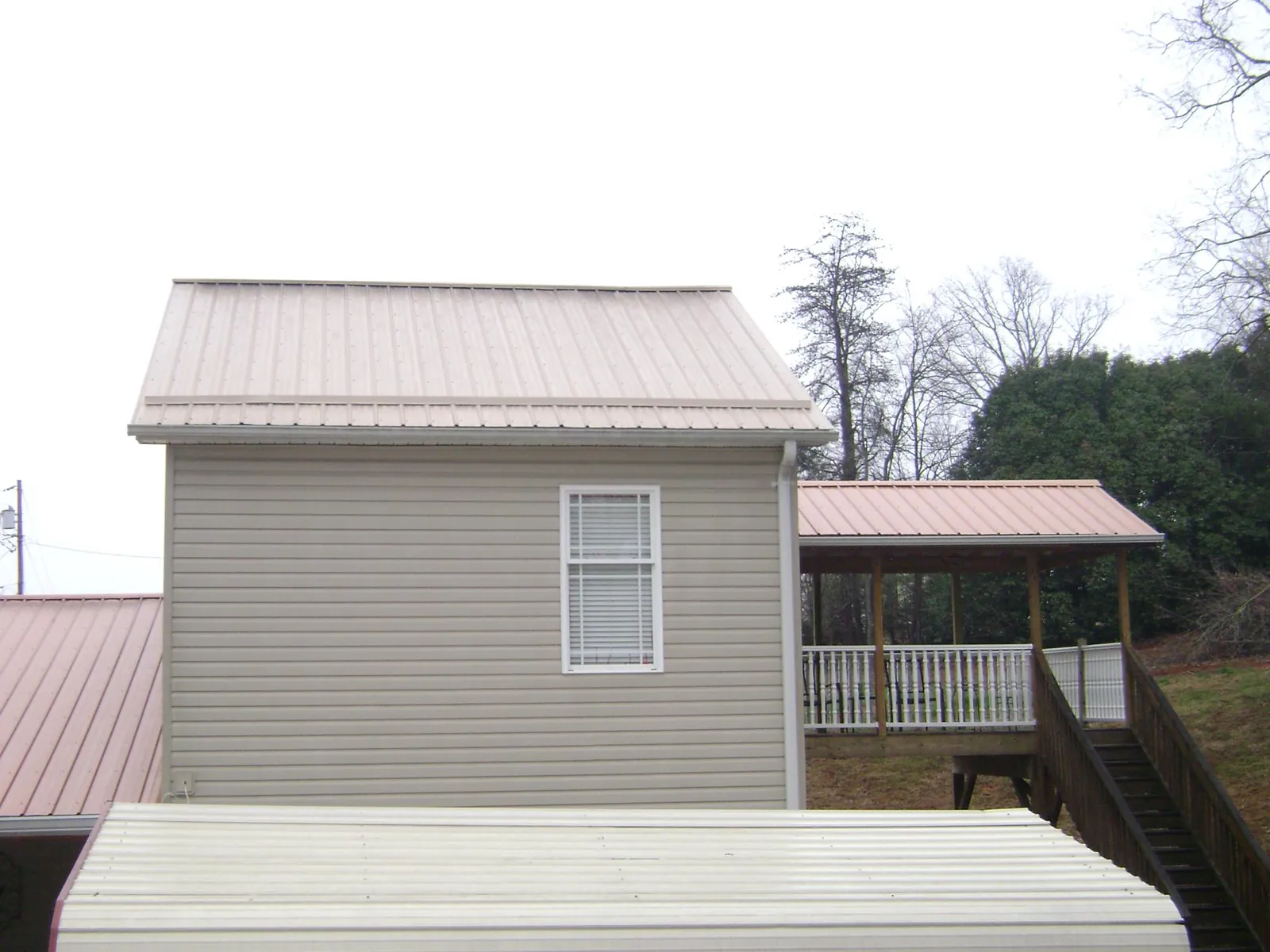 Tan metal roofs on a two story addition and attached porch, from a Roof Replacement job in Canute